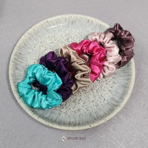 Silk scrunchies in turquoise, purple, champagne, bright pink, blush, and brown arranged on a decorative plate